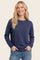 woman wearing a navy blue long sleeve sweater with a crew neckline and side slits, smiling and hands in pockets
