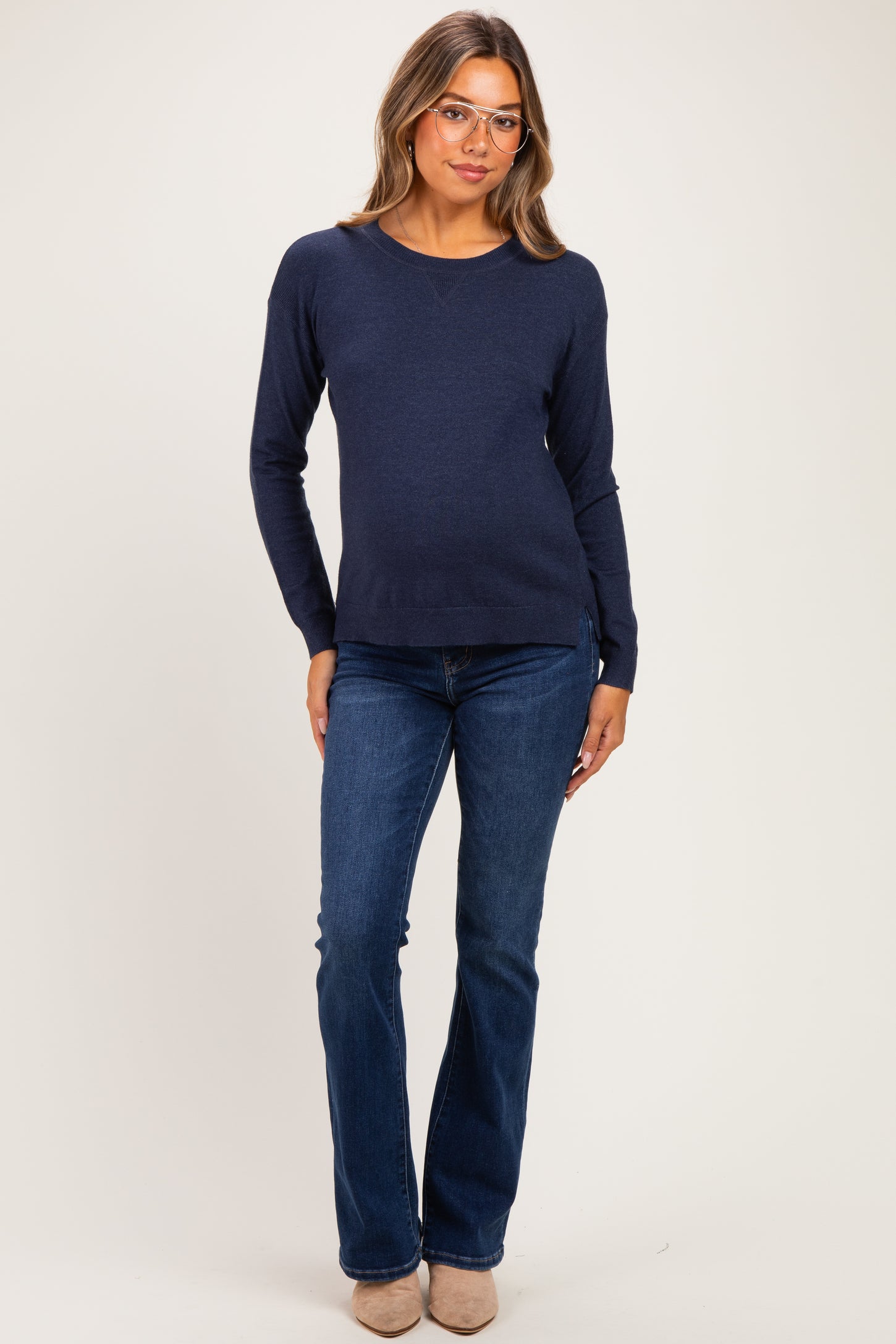 woman wearing a navy blue maternity sweater and dark blue flared jeans with a visible baby bump