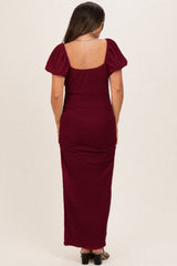 woman wearing a burgundy maternity maxi dress with puff sleeves, showing a smooth back profile