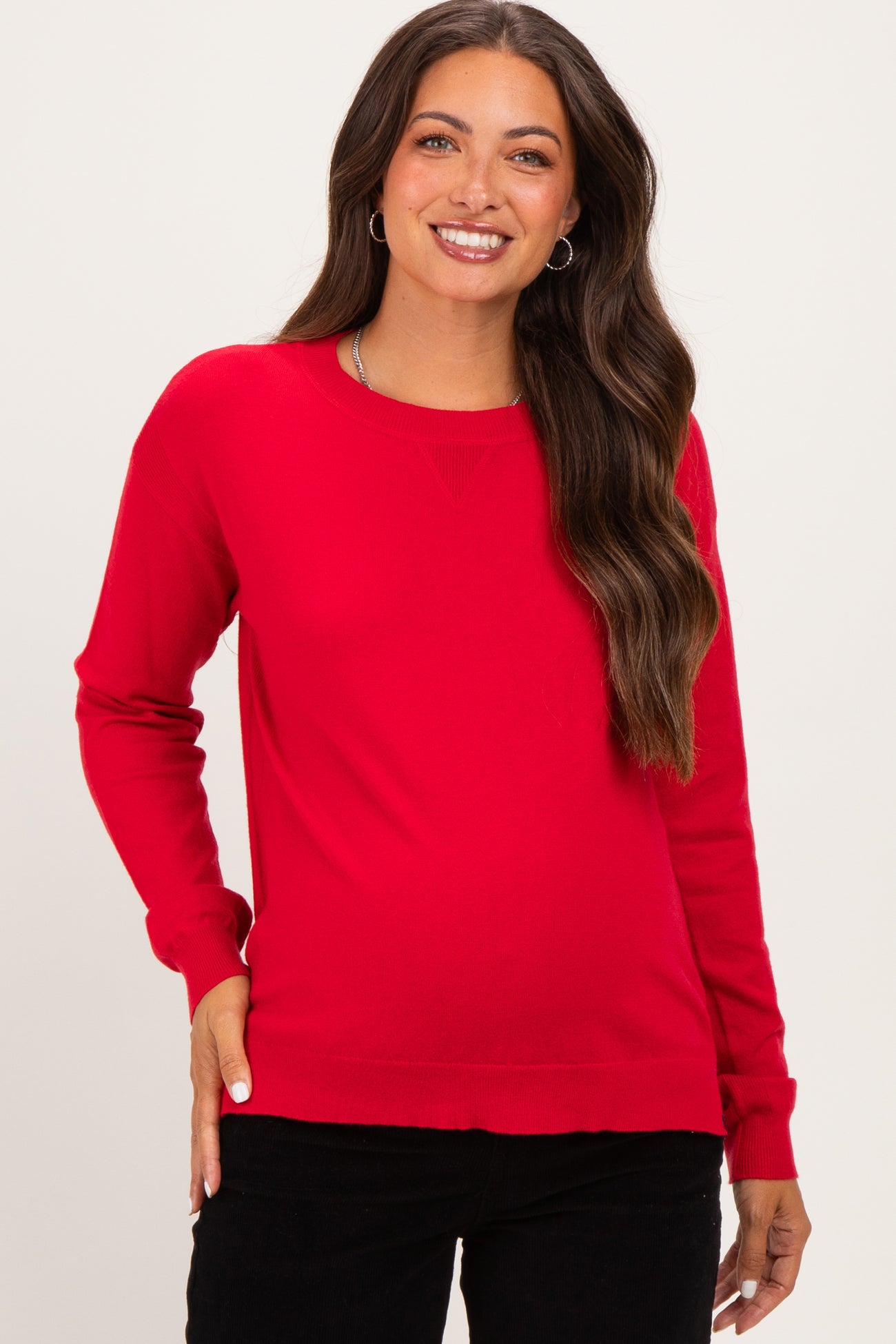 woman wearing a bright red long sleeve maternity sweater with a relaxed fit and smiling at the camera