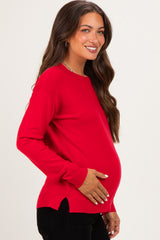 woman wearing a red long sleeve maternity top and holding her baby bump