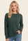 woman wearing a dark green long sleeve sweater and blue jeans, smiling with one hand in her pocket