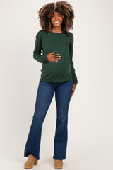 woman wearing a dark green maternity sweatshirt and blue flared jeans, holding her baby bump