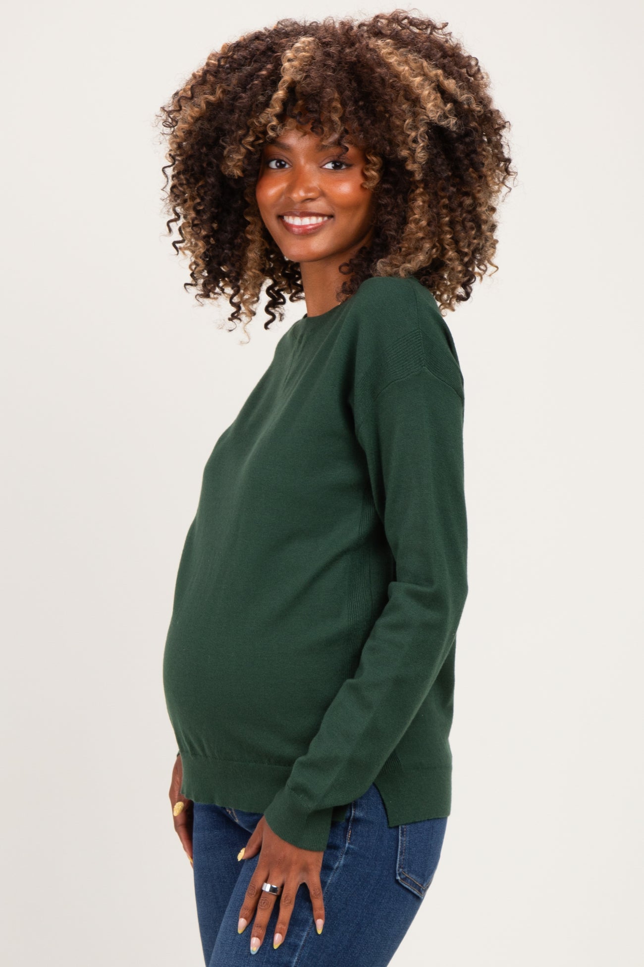 woman wearing a dark green maternity sweater and showing her baby bump