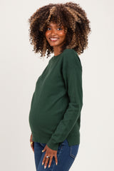 woman wearing a dark green maternity sweater and showing her baby bump