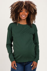 woman wearing a dark green long sleeve maternity sweater and smiling while showing her baby bump