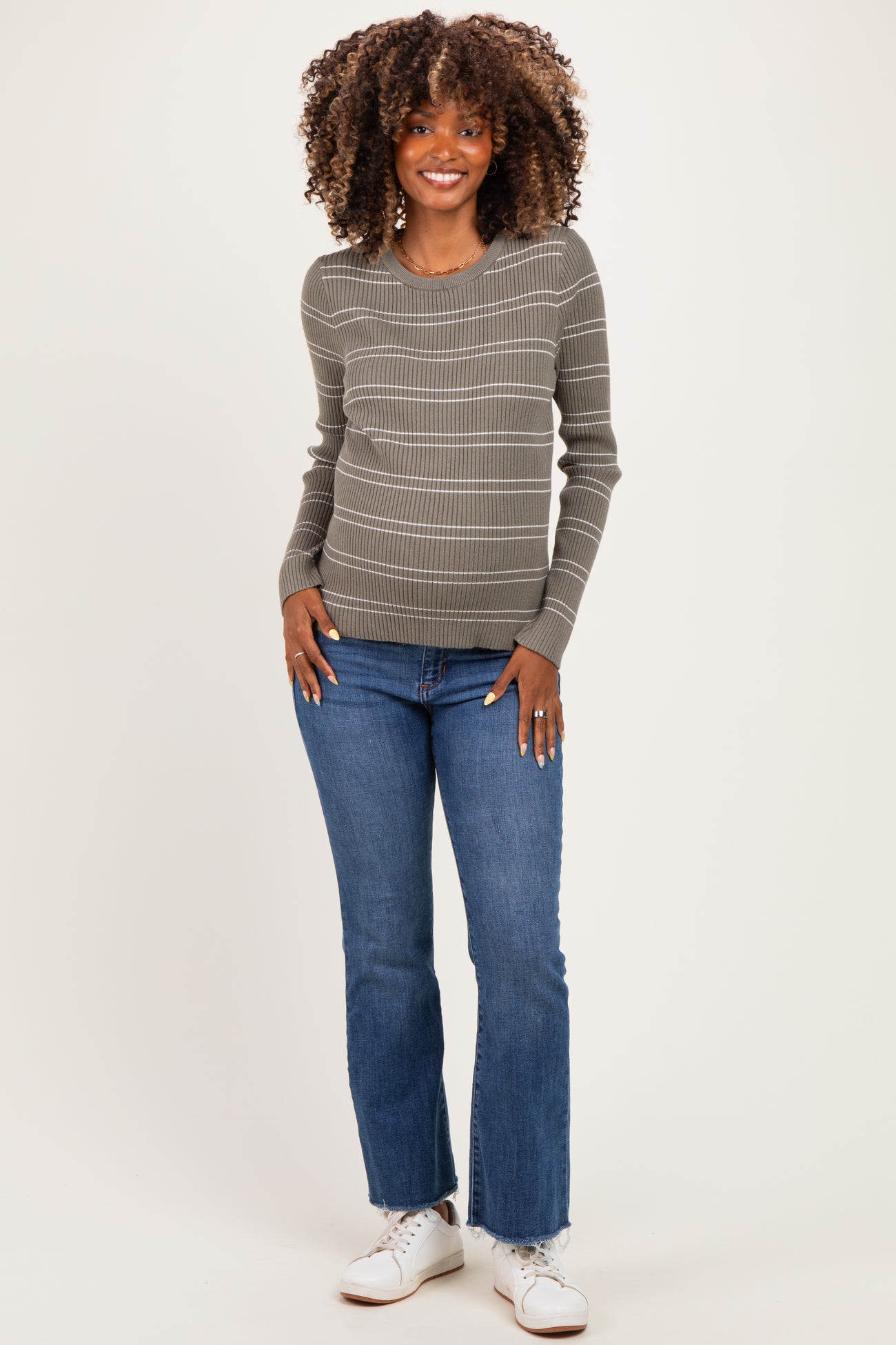 woman wearing a grey striped maternity sweater and blue jeans, showing her baby bump