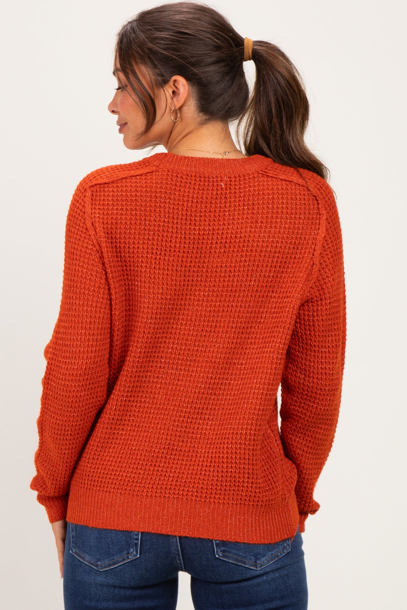 woman wearing an orange textured maternity sweater, viewed from the back, with a ponytail and casual jeans