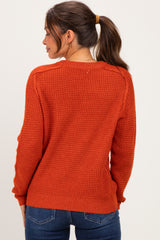 woman wearing an orange textured maternity sweater, viewed from the back, with a ponytail and casual jeans