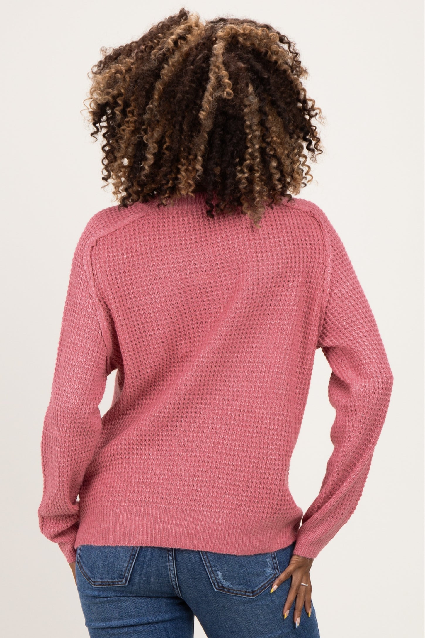 woman wearing a pink knit maternity sweater, viewed from the back, with long sleeves and a relaxed fit