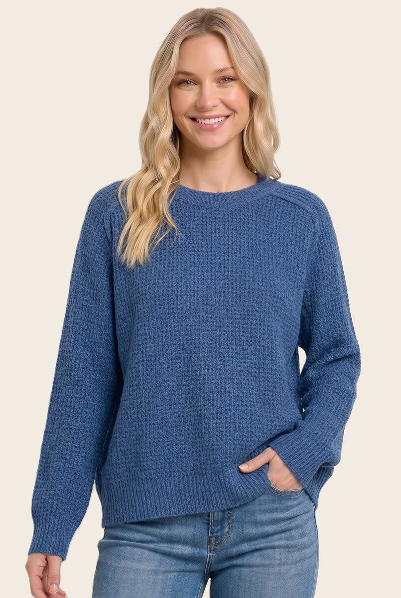 woman wearing a blue textured sweater with a relaxed fit and long sleeves, smiling and posing with her hands in her pockets