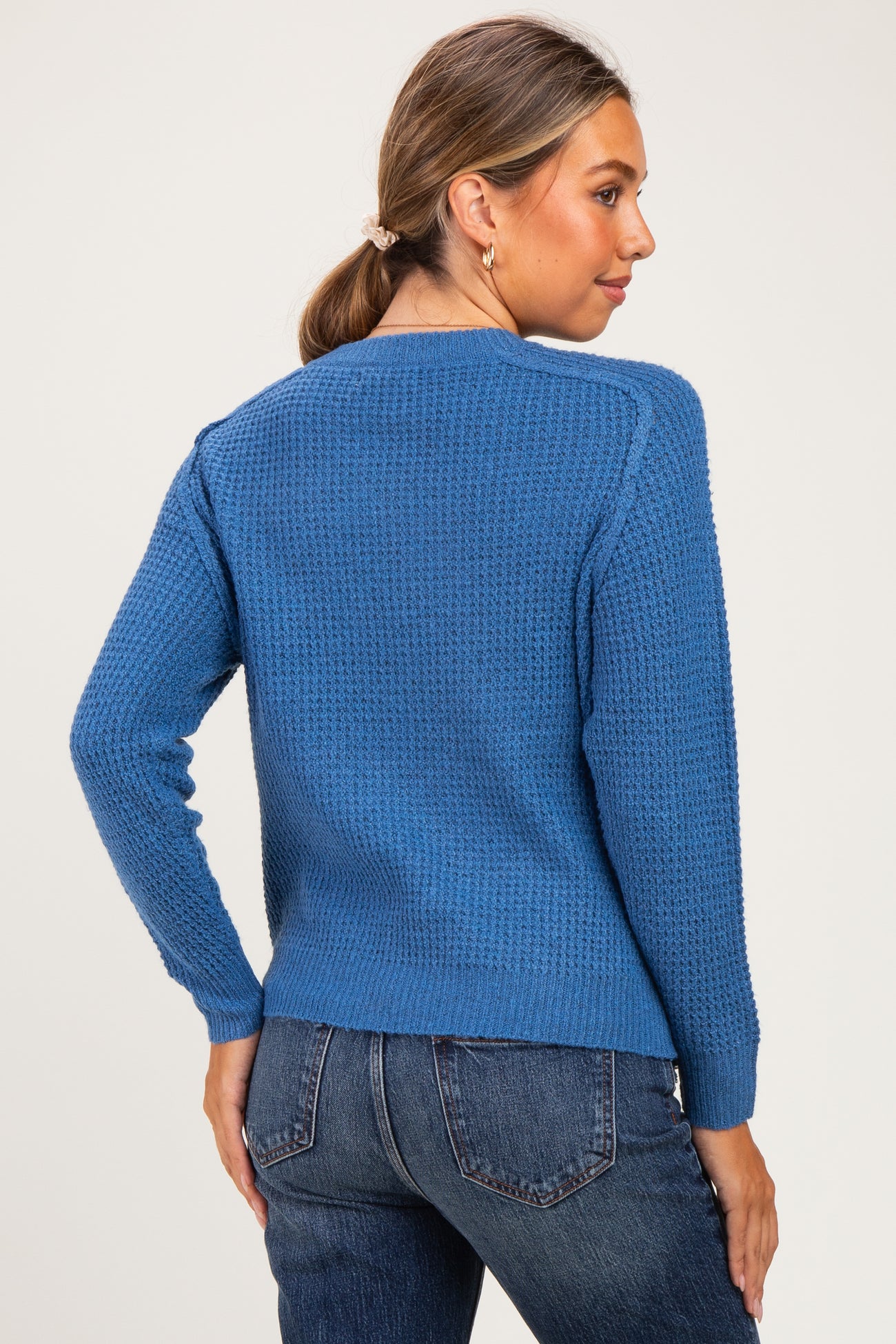 woman wearing a blue textured maternity sweater with long sleeves, seen from the back.