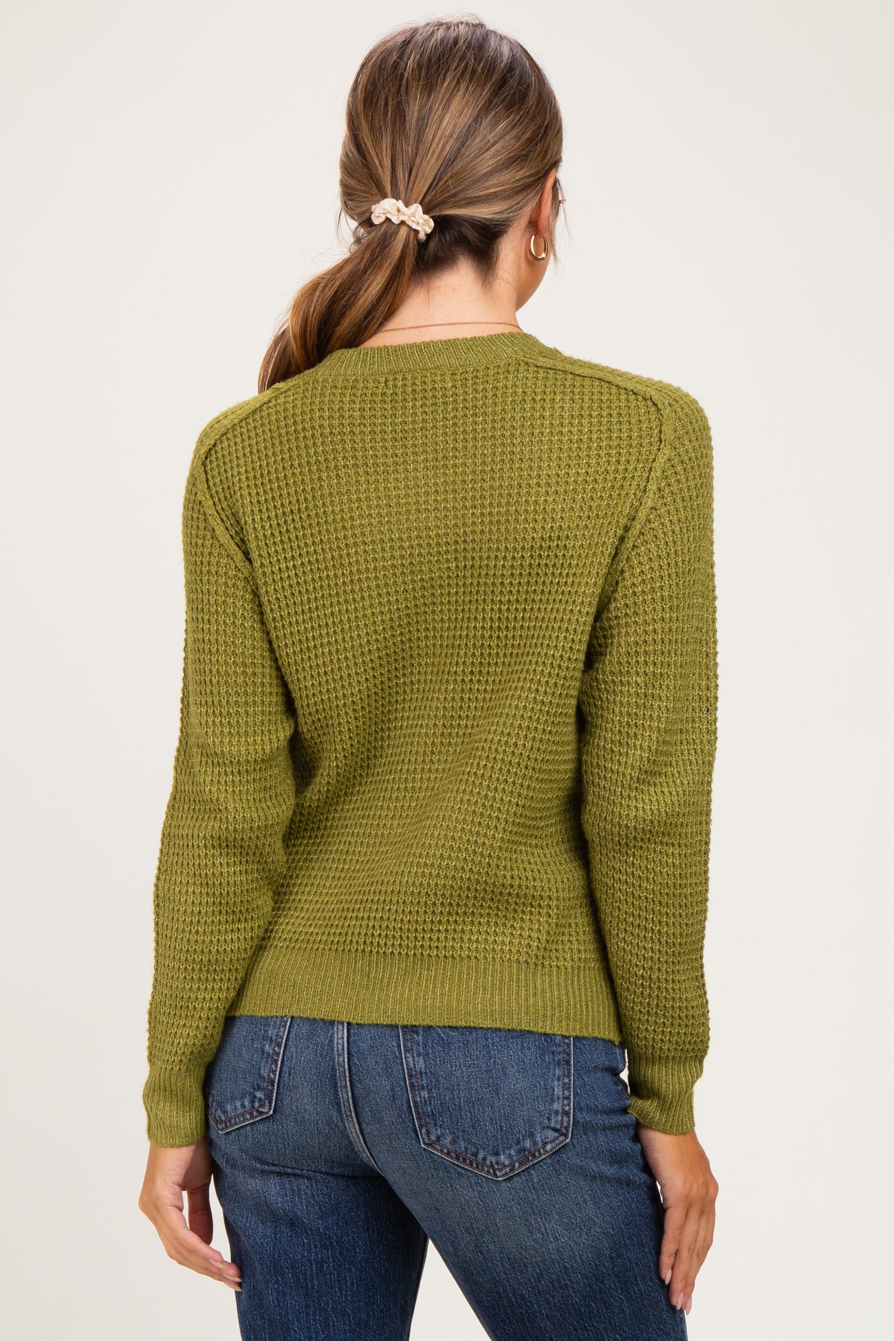 woman wearing an olive green waffle knit maternity sweater with a round neckline and long sleeves, styled with blue jeans