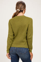 woman wearing an olive green waffle knit maternity sweater with a round neckline and long sleeves, styled with blue jeans