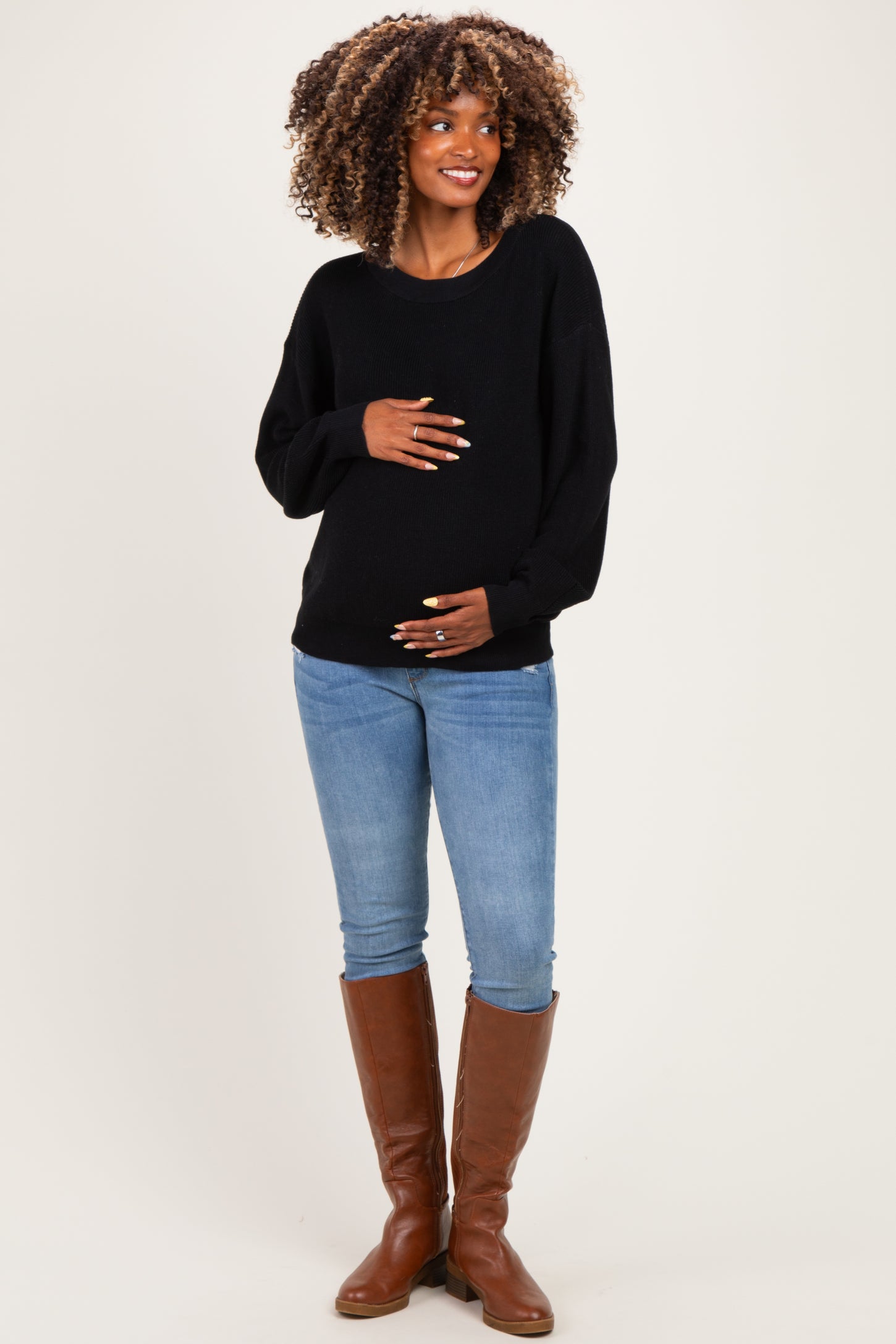 woman wearing a black maternity sweater and blue jeans, holding her baby bump and smiling