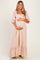 woman wearing a blush floral maternity maxi dress with puff sleeves and ruffled hem, holding her baby bump