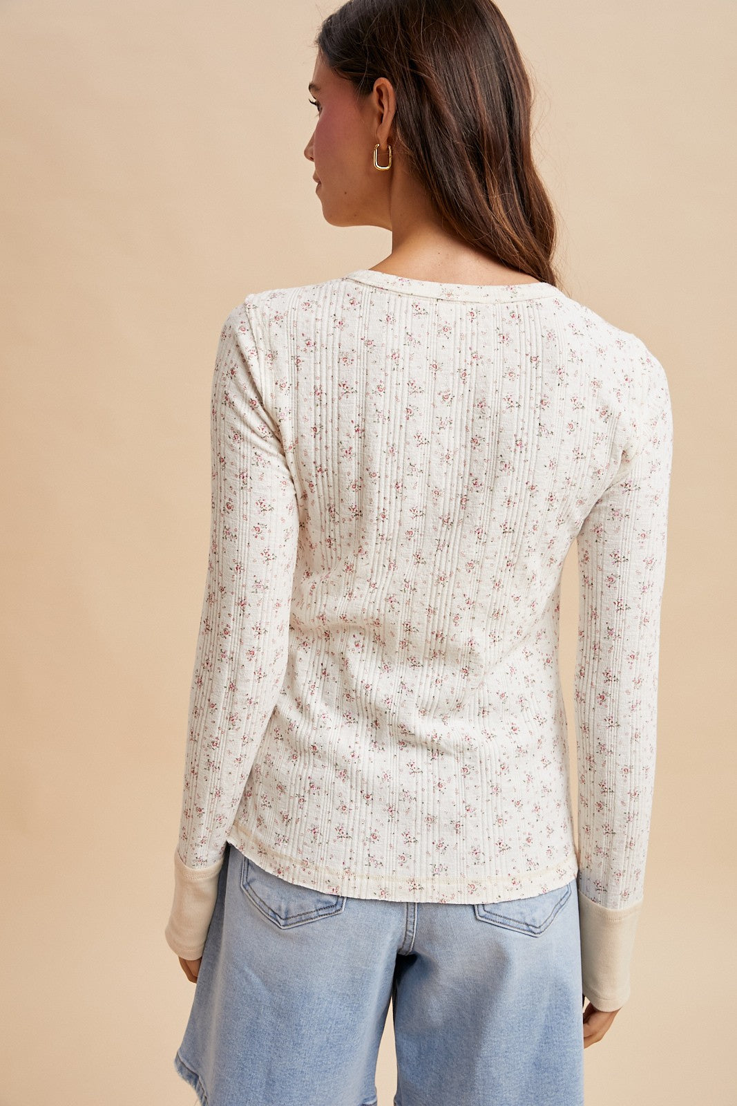 woman wearing a cream long sleeve top with delicate floral print and ribbed texture, styled with light blue denim shorts