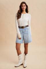 woman wearing a cream long sleeve button-up top with floral print and light blue denim shorts, paired with white cowboy boots