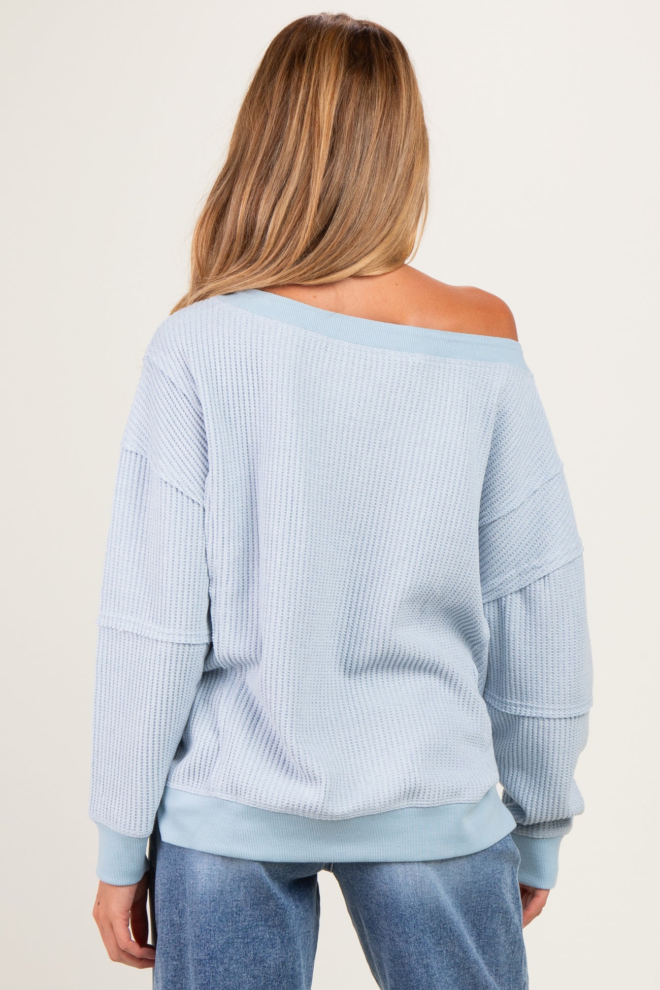 woman wearing a light blue off-the-shoulder maternity sweater with a relaxed fit and long sleeves