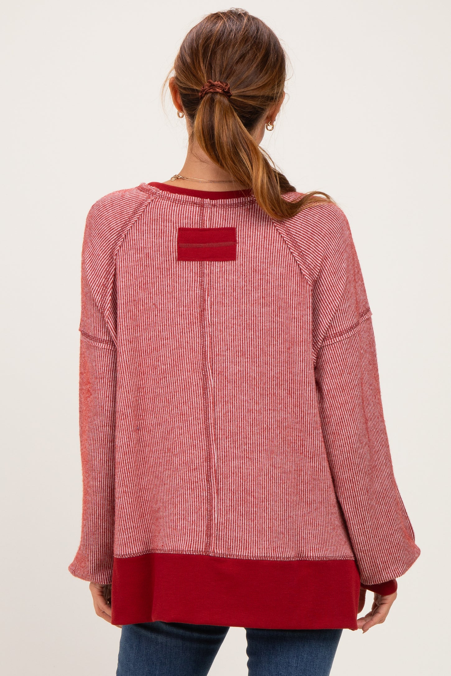 woman wearing a red striped oversized sweater with a solid red hem and back detail, styled with jeans