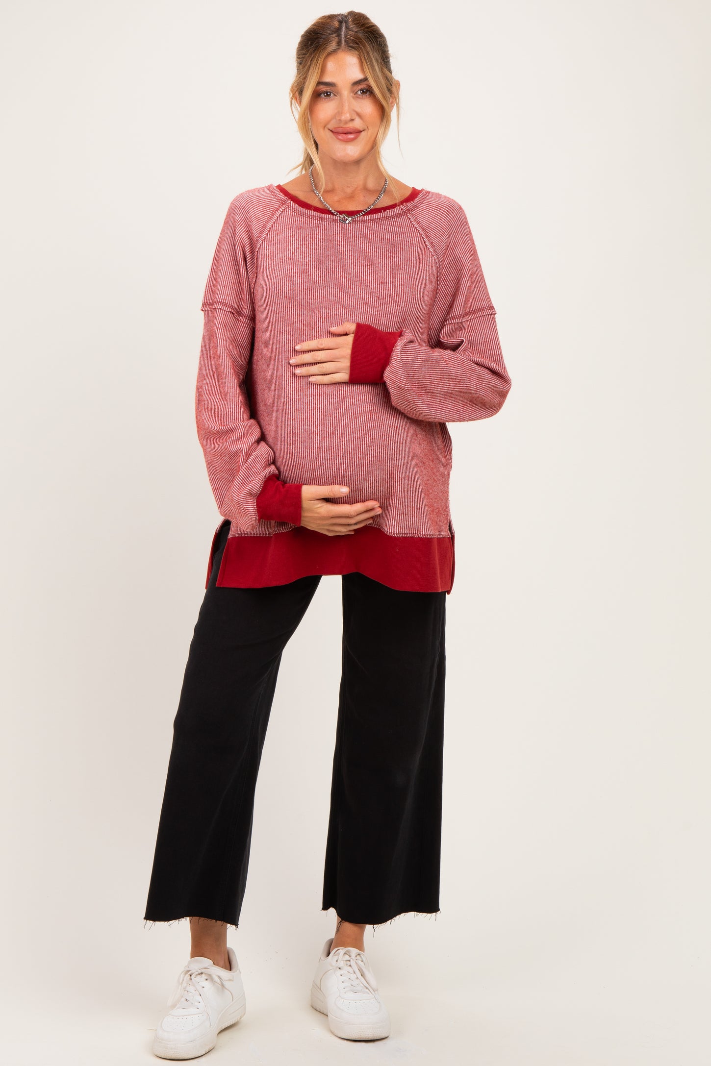 woman wearing a red and white striped maternity sweater, holding her baby bump, paired with black wide-leg pants