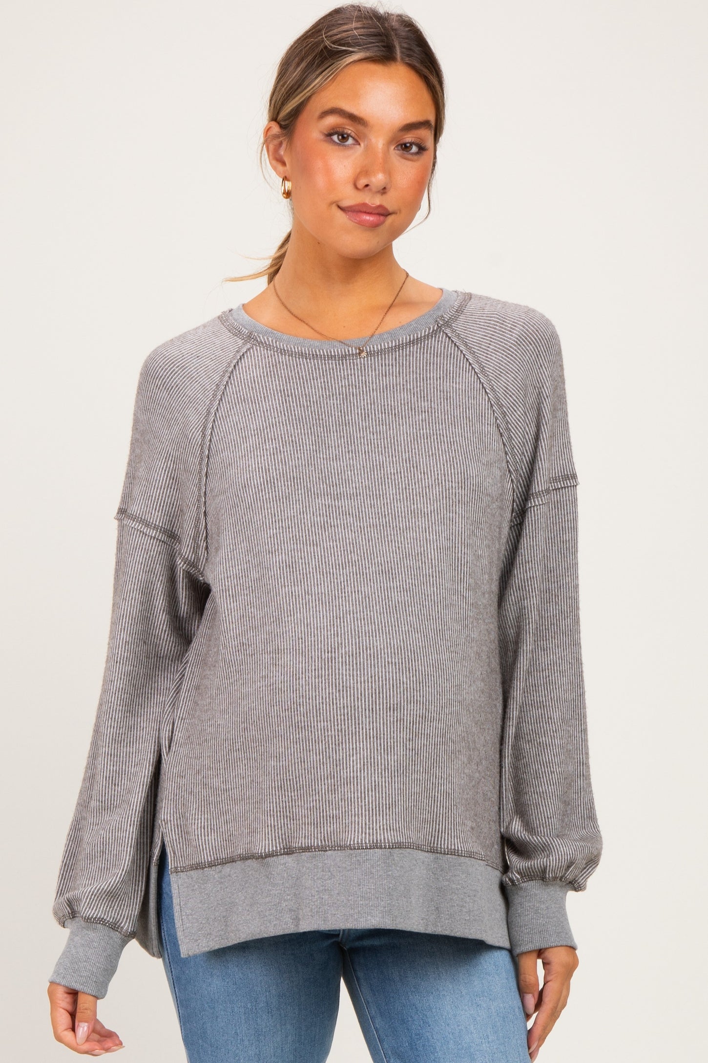 woman wearing a gray striped maternity sweater with long sleeves and side slits, styled with blue jeans