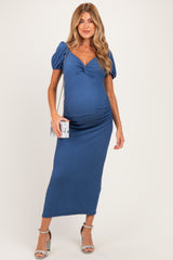 woman wearing a blue maternity dress with puff sleeves and a gathered front, holding a small purse and showing her baby bump
