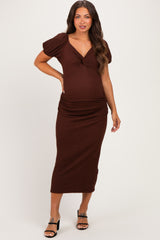 woman wearing a brown smocked maternity dress with short puff sleeves and a knot detail, showing her baby bump