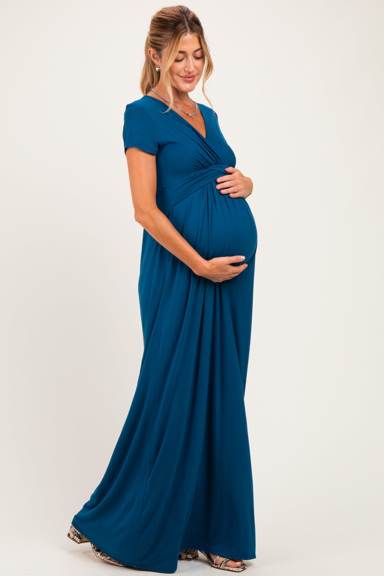 woman wearing a teal maternity maxi dress with a v-neck and gathered detail, holding her baby bump