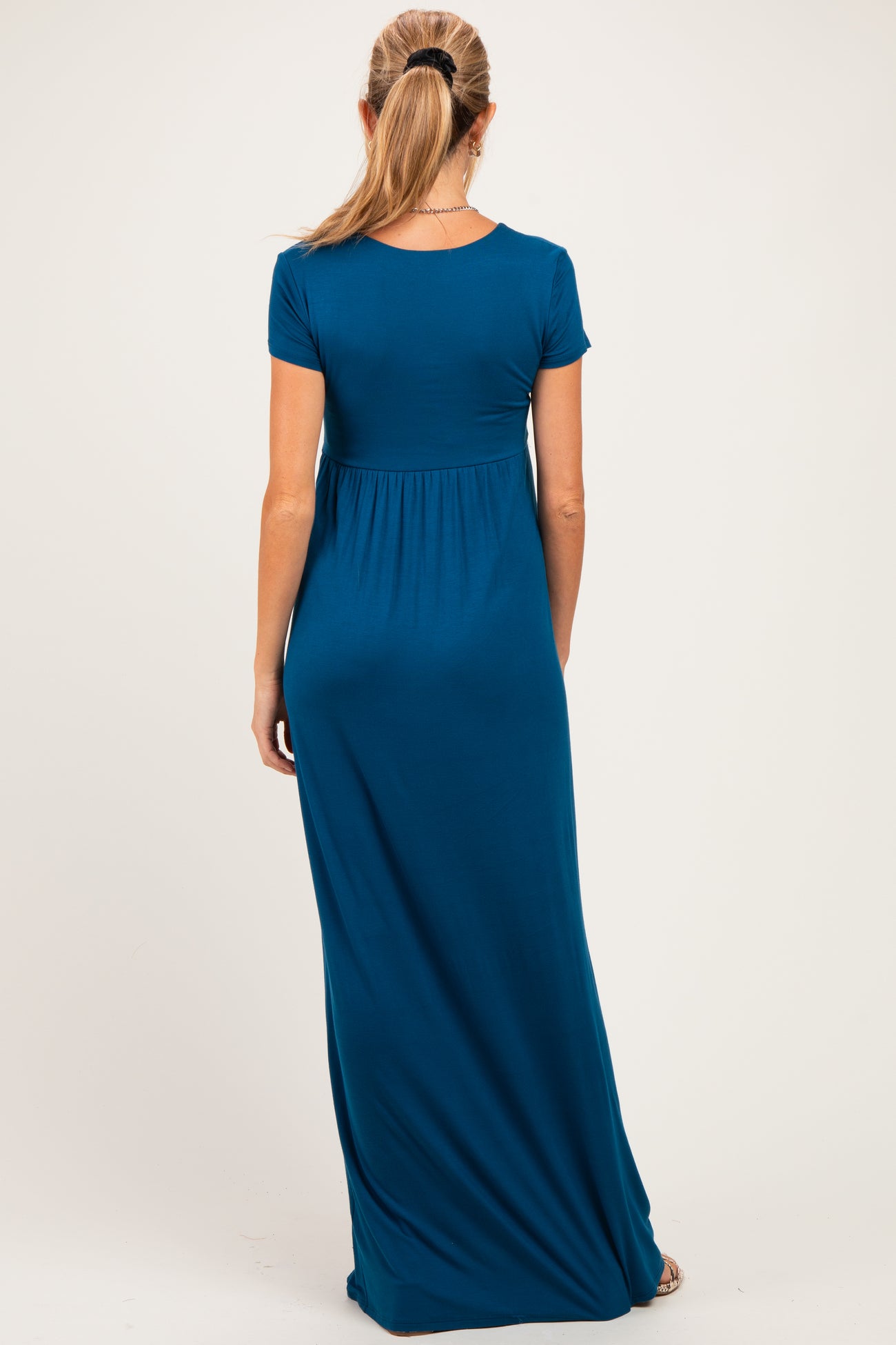 woman wearing a teal short sleeve maternity maxi dress, showing the back view and a gathered waistline