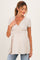 woman wearing a light beige short sleeve maternity top with a wrap design and visible baby bump, paired with jeans