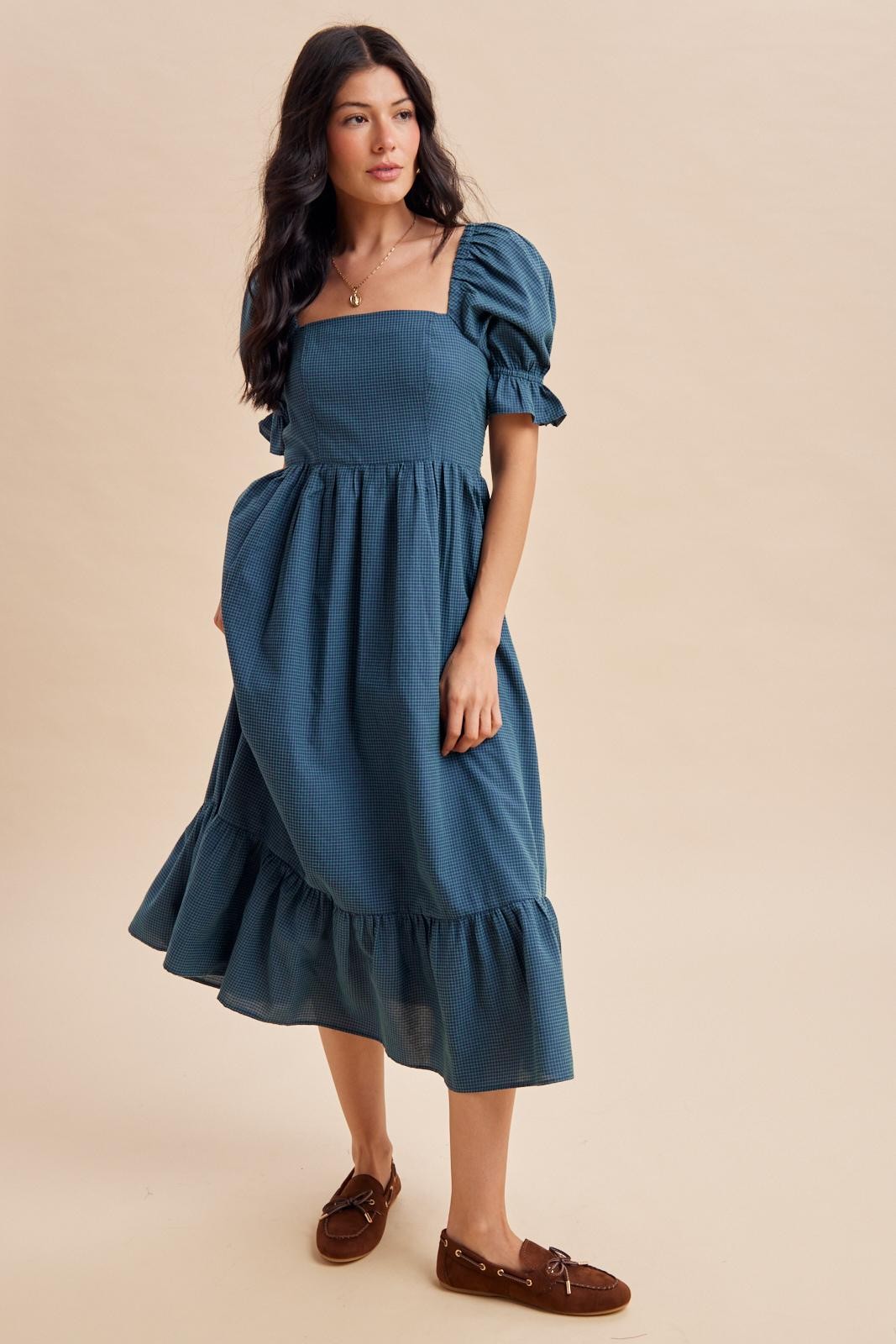 woman wearing a blue checkered midi dress with puff sleeves and a ruffled hem, paired with brown slip-on shoes