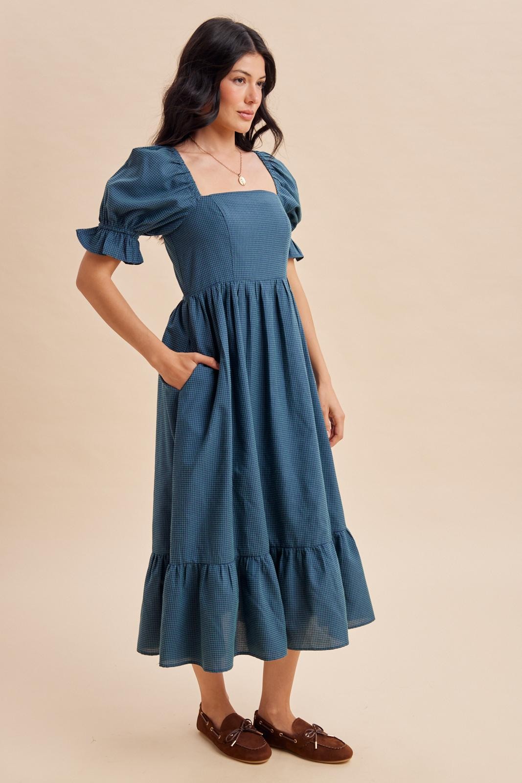 woman wearing a teal midi dress with puff sleeves and a ruffled hem, featuring pockets and a square neckline