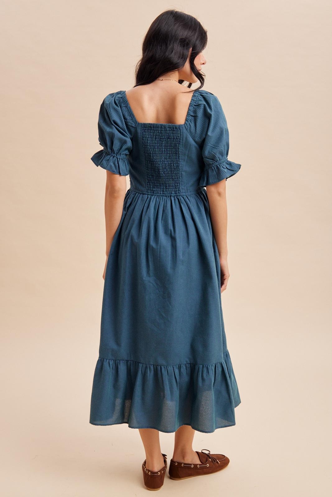 woman wearing a teal blue midi dress with puff sleeves and a ruffled hem, viewed from the back