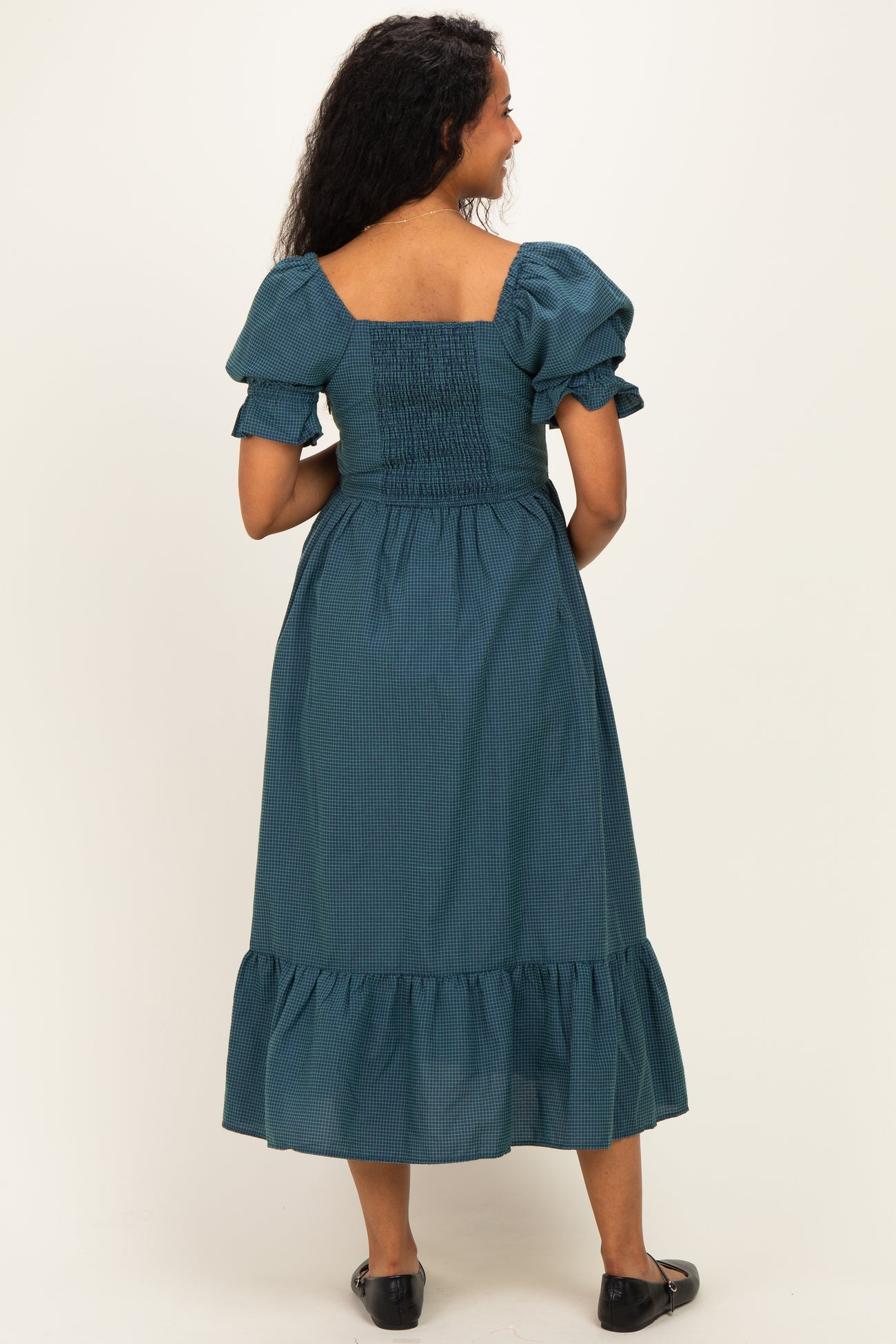 woman wearing a teal maternity dress with puff sleeves and a ruffled hem, showing the back view