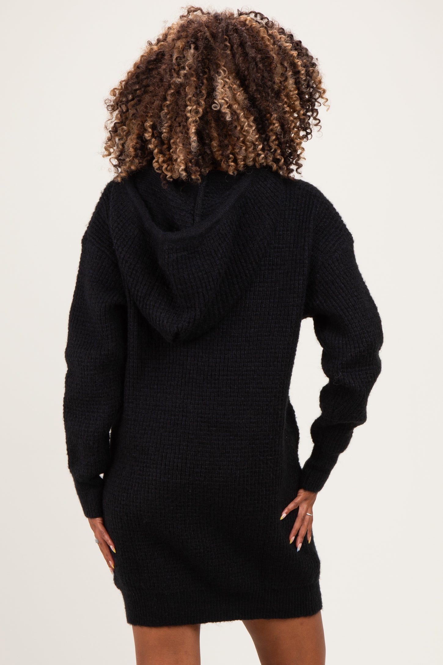 woman wearing a black knitted maternity hoodie dress, showing a relaxed fit and hood in the back