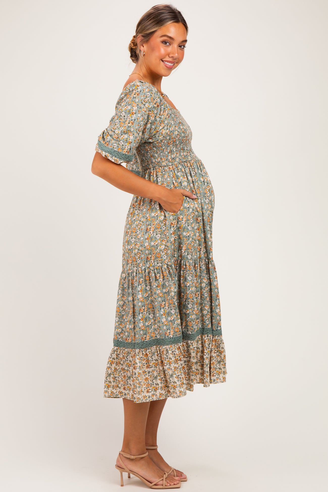woman wearing a green floral maternity dress with pockets and tiered hem, highlighting her baby bump