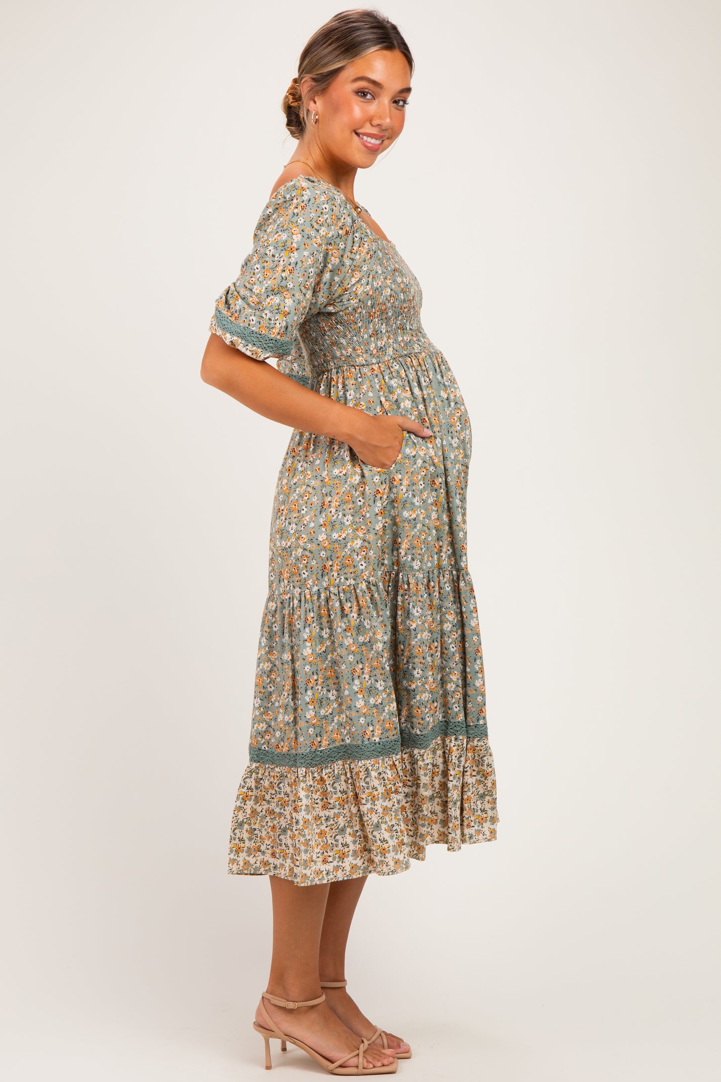 woman wearing a green floral maternity dress with pockets and tiered hem, highlighting her baby bump