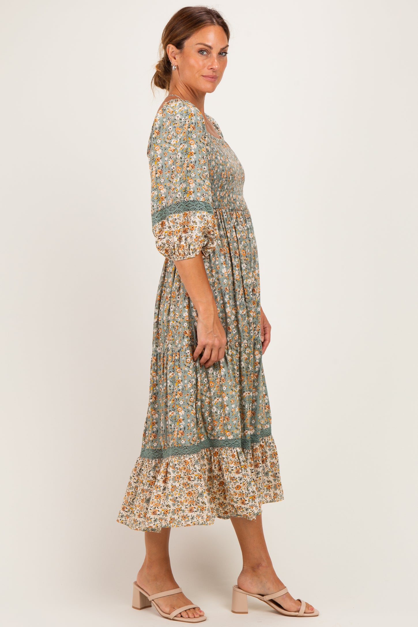 woman wearing a green floral midi dress with puff sleeves and a tiered hem, paired with beige slide sandals