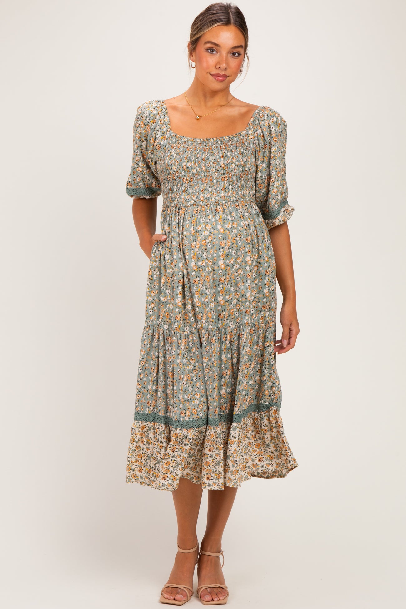 woman wearing a green floral maternity dress with puff sleeves and a ruffled hem, smiling and posing casually