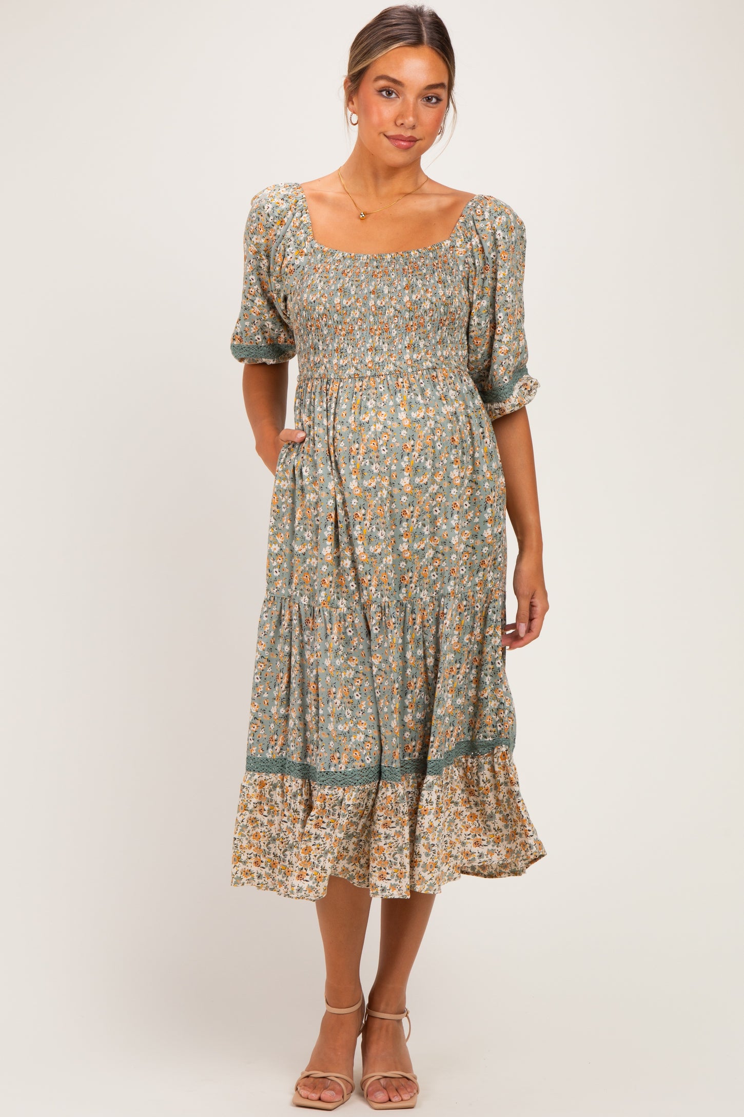 woman wearing a green floral maternity dress with puff sleeves and a ruffled hem, smiling and posing casually