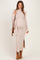 woman wearing a light beige ribbed maternity maxi dress with a side slit and a matching long cardigan, holding a brown purse and showing her baby bump