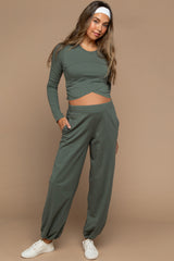 woman wearing a green maternity long sleeve top with a twist front and matching jogger pants, showing her baby bump