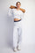 woman wearing a white cropped long sleeve top and light gray sweatpants, holding a yoga mat over her shoulders