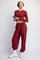 woman wearing a burgundy long sleeve crop top and matching jogger pants, holding a phone and wearing headphones