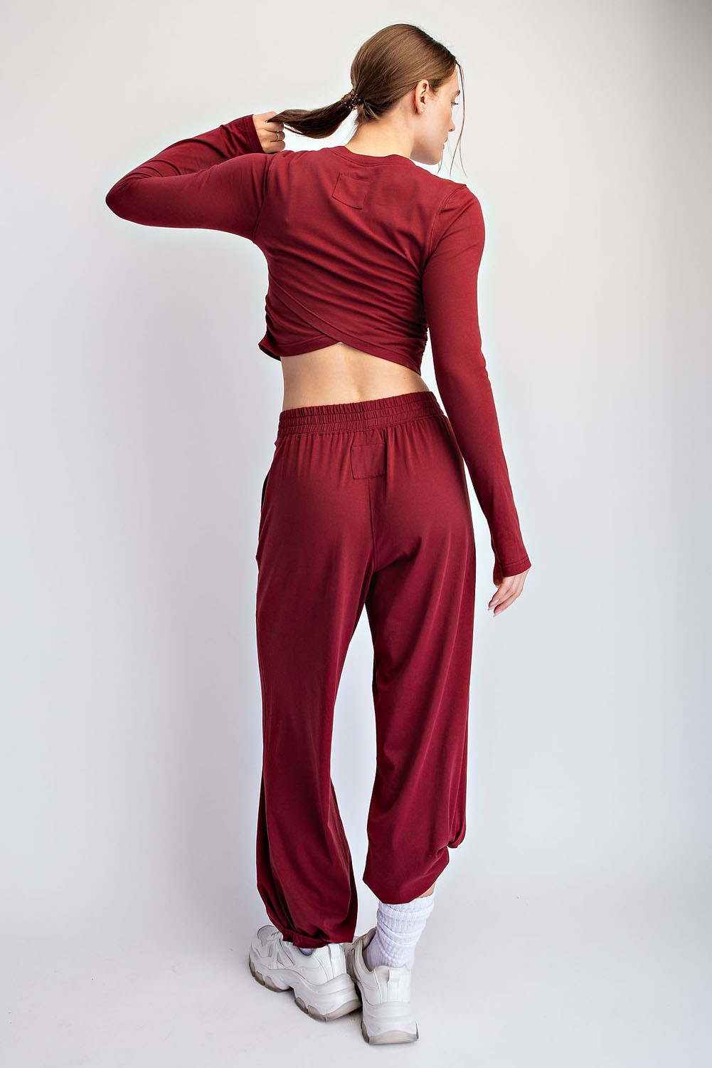 woman wearing a burgundy long sleeve crop top and matching jogger pants, showing the back view with white sneakers