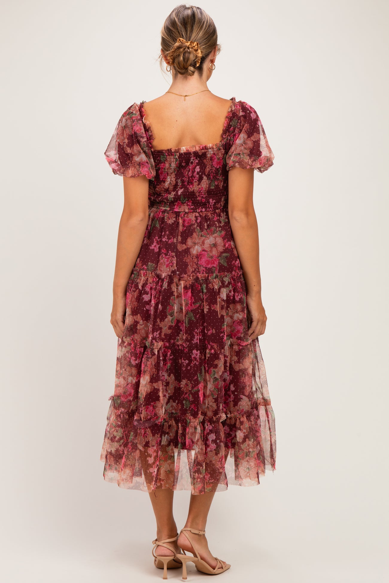 woman wearing a floral burgundy maternity dress with short puff sleeves and a tiered skirt, showing a baby bump from behind