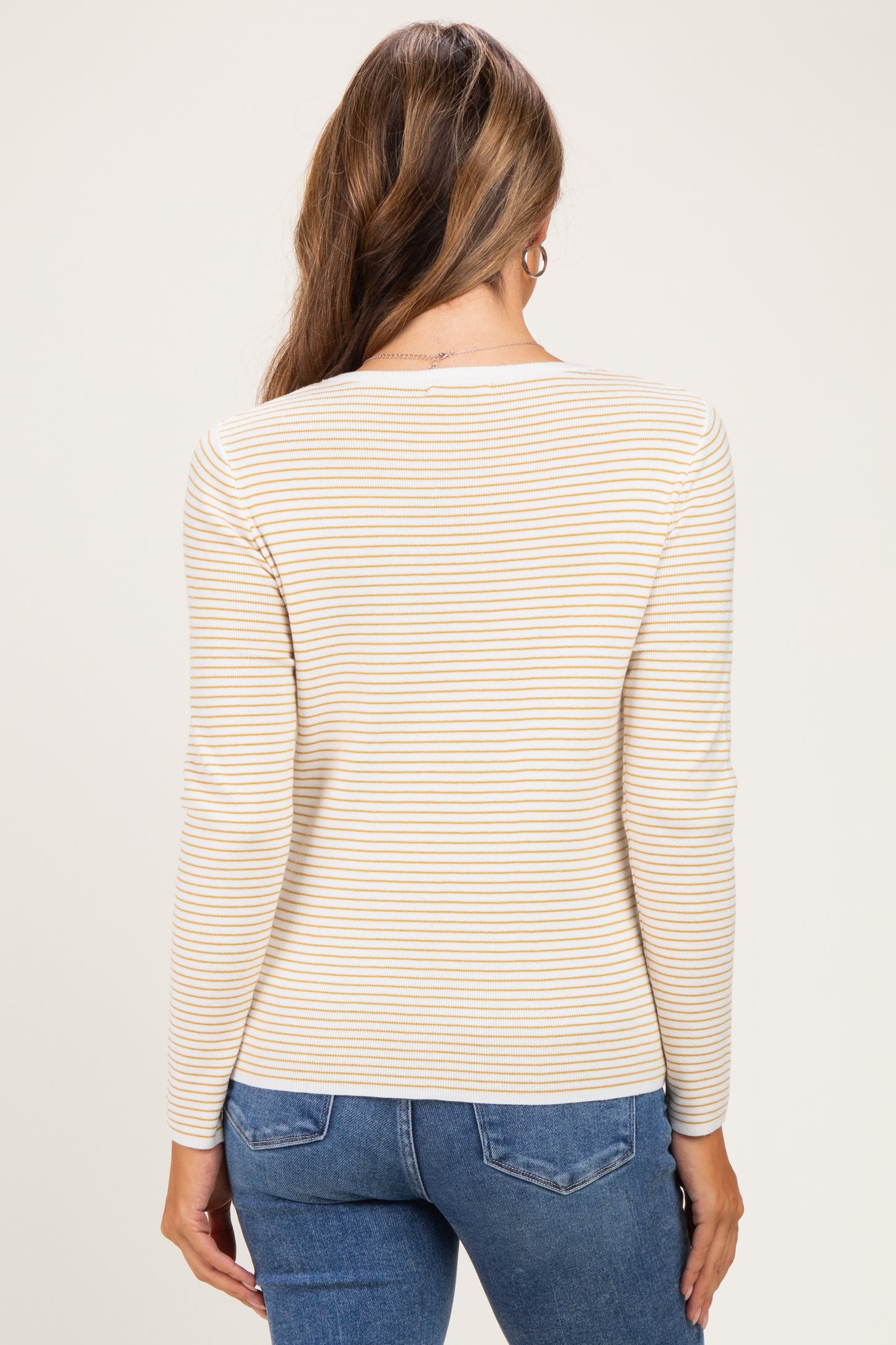 woman wearing a cream and yellow striped long sleeve maternity top, shown from the back with casual blue jeans