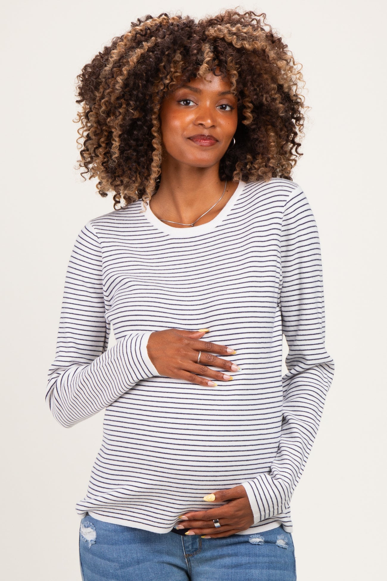 woman wearing a gray and white striped long sleeve maternity top and holding her baby bump