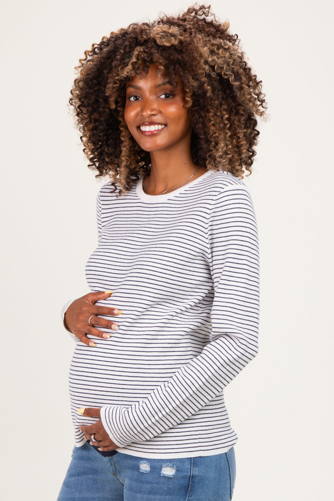 woman wearing a gray and white striped maternity top and holding her baby bump with a smile